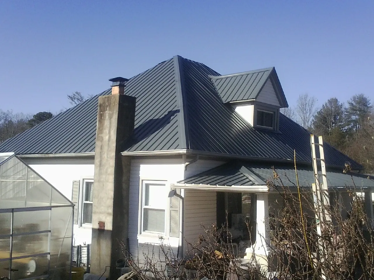 Dark blue standing seam metal roof on a white farmhouse with dormer — Slate & Tile Roof Repair by Roofing Brothers in Pandora