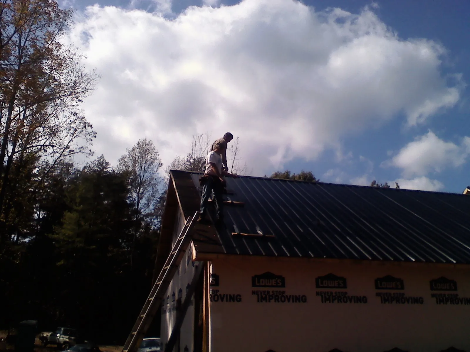 Roofer fastening dark metal panels high against a cloudy sky, from a Roof Inspection job in Pandora