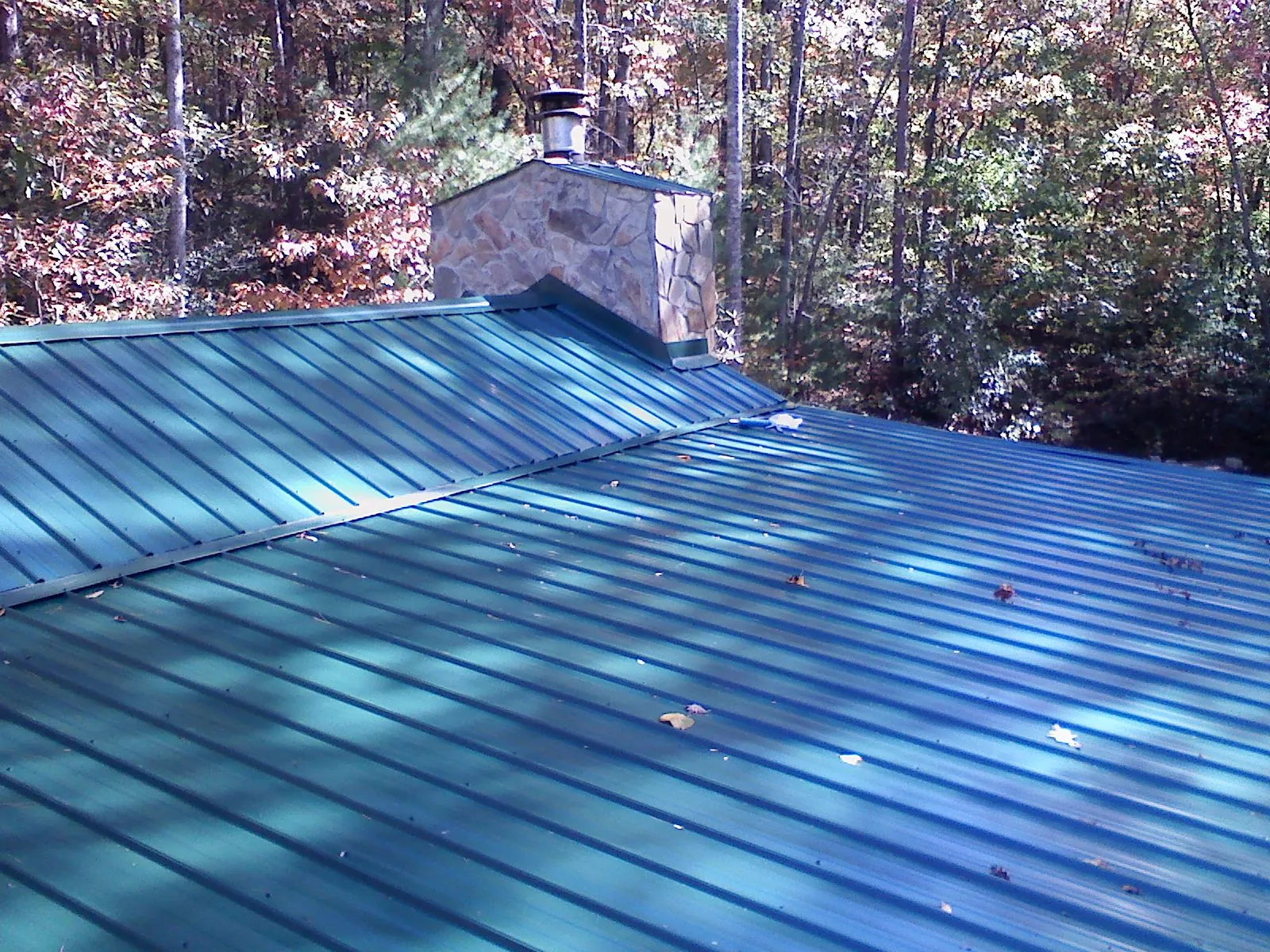 New green metal roof and stone chimney surrounded by autumn woods in Pandora
