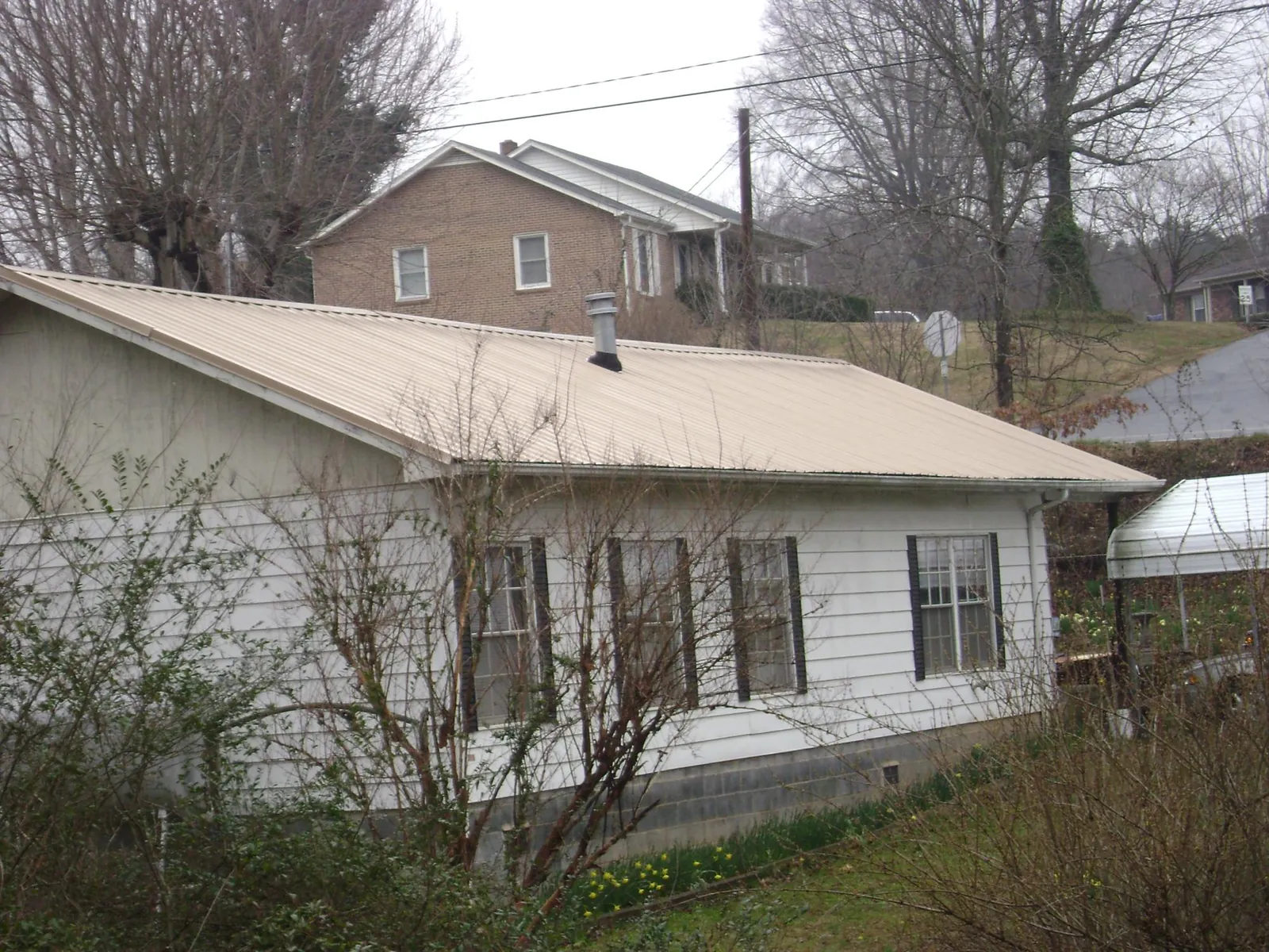 Tan metal roof on a white sided house set into a hillside — Commercial Roofing by Roofing Brothers in Pandora